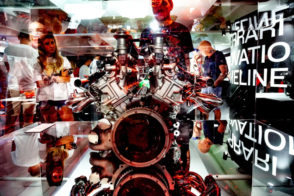Moteur Ferrari exposé, reflets des visiteurs dans la vitrine