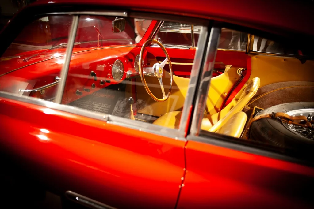 Ferrari rouge, l'habitacle et le volant en bois vus par la vitre