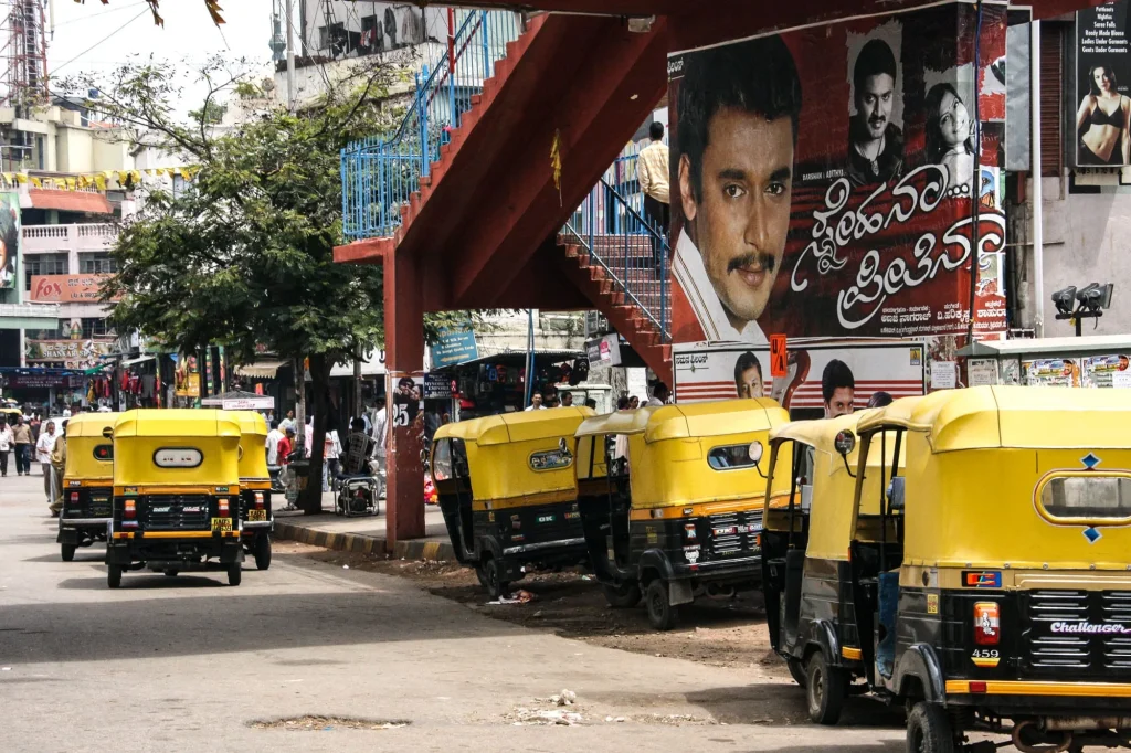 Rickshaws jaunes alignés sous une affiche de cinéma, en Inde